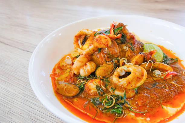 Stir fried chilli, shrimp, squid, sea shells wrapped in thick eggs in a white dish on a wooden background.