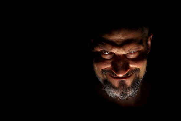 istock Face with a bearded man grimace against a dark background with sharp shadows. Comedic, fabulous villain or negative character conception with copy space. 1156366925