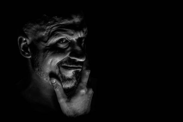 istock Face with a bearded man grimace against a dark background with sharp shadows. Comedic, fabulous villain or negative character conception with copy space. 1156366982