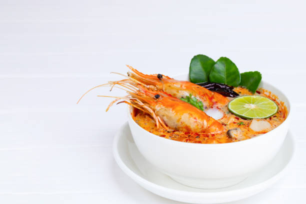 tom yum goong ou soupe de crevettes soupe aigre soupe traditionnelle en thaïlande contient chili, lime, gingembre, galangal, citronnelle, feuille de lime, vue du haut sur un fond de bois blanc. - sour taste green traditional culture lemon photos et images de collection