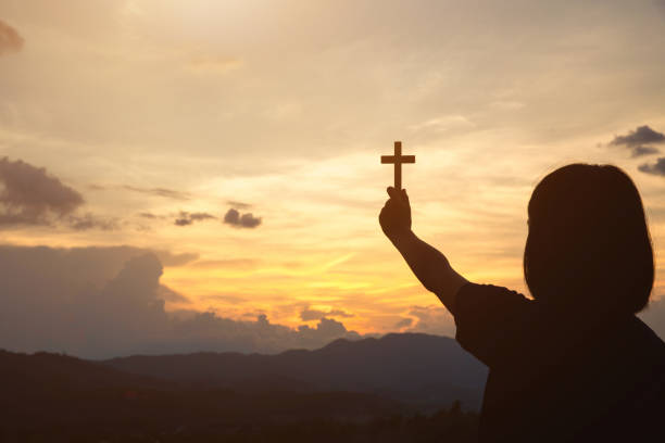 hand of a girl holding a cross at sunrise, eucharist therapy bless god helping repent catholic easter lent mind pray. prayer to god christian religion concept background. - praying human hand worshipper wood imagens e fotografias de stock