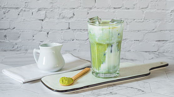 Matcha green tea latte with matcha powder and wooden spoon . Grey background. Copy space.