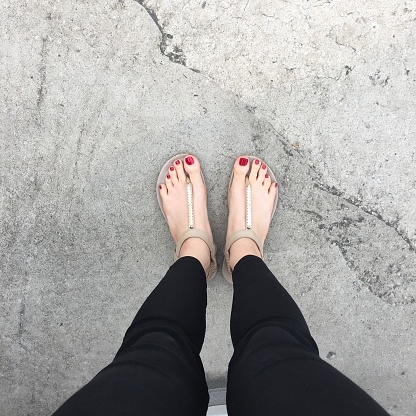 Selfie Shoes Isolated on Top View. Red Nails Manicure. Woman Wearing Gold Slippers (Flip-Flop) on Cement