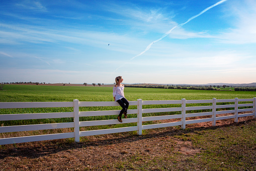 Smiling woman sitting on rural farm fence of agricultural fields in country NSW