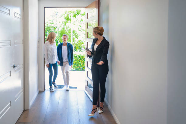 Real estate agent showing a young couple a new house. Real estate agent showing a young couple a new house. The house is contemporary. All are happy and smiling. The couple are casually dressed and the agent is in a suit. The couple are being greeted at the front door by the real estate agent. Copy space show home stock pictures, royalty-free photos & images