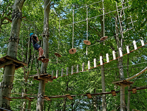 Hoherodskopf, Germany - June 15, 2019: A man in a ropes course / high-ropes garden / Klettergarten in Germany. He is climbing and balancing at different elements of hanging balancing devices.
