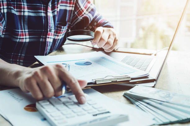 istock Business man using magnifying to review balance sheet annual with using calculator and laptop computer to calculating budget. audit and Check integrity before investment concept. 1156389990