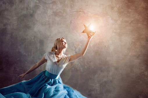 Shining star in hand, reach for the dream concept. Young woman holding a star in her hand, dreams and goals, concept