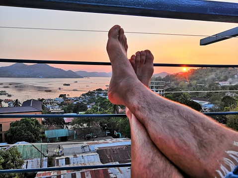 Feet of Man relayeing in one of the rooftop bars for tourists enjoying the View of Coron from Mt Tapyas during a beautiful sunset