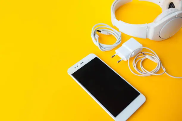 Mobile kit with smartphone, headphones and chargers. Yellow background, Copy space to the left