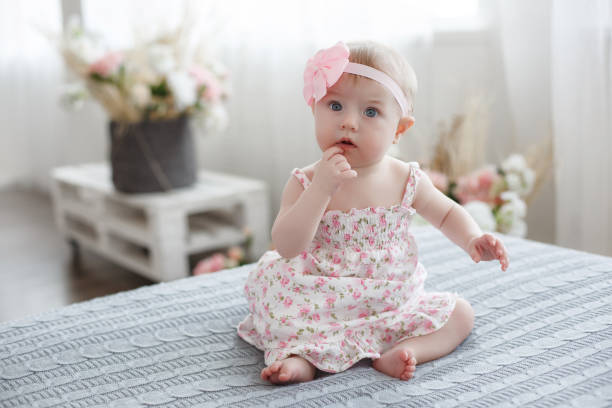 Adorable baby boy in white sunny bedroom plays alone on the bed. Charming beautiful lovely small female baby with plump cheeks creeps on bed, looks innocently on something, being naughty. Cute baby infant plays alone. Newborn kid crawls. Enthusiastic child only baby girls stock pictures, royalty-free photos & images