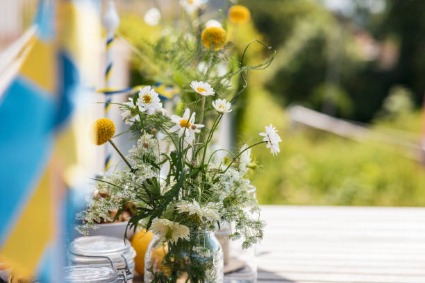 Midsummer celebration Flowers on a table with the Swedish flag in the front of it. summer solstice stock pictures, royalty-free photos & images