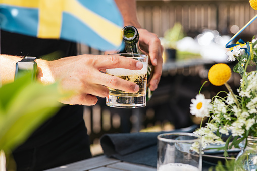 Swedish midsummer celebration. A man is pouring beer into a glass. The Swedish flag can be seen in the right corner of the photo.