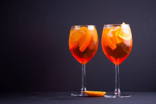 Cocktail Spritz on black background. Summer alcohol cocktail with orange fruit and fresh mint. Italian cocktail Spritz on wooden boards