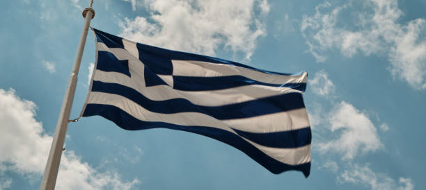 istock greece flag in a windy and sunny day against clear blue sky with clouds. 1156409329