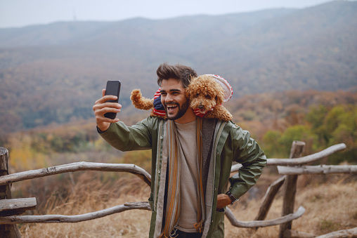 Smiling attractive mixed race man in raincoat taking selfie with his dog. Autumn time.