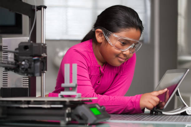 A young student wearing pink is working on a touchscreen making changes to a 3d printed toy in a summer school tech class. stock photo