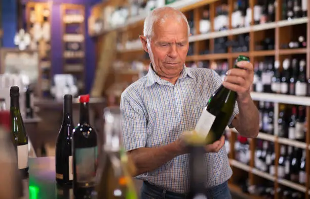 Senior male visiting winehouse in search of bottle of good wine