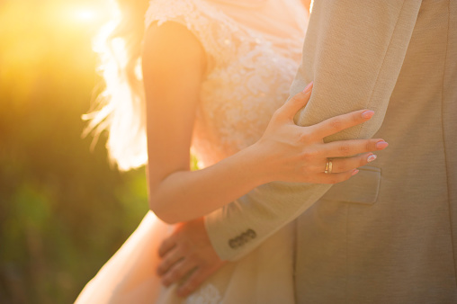 Photo of a wedding couple in the summer. Bride and groom hugging, hands, rings, wedding bouquet close-up and copy space.