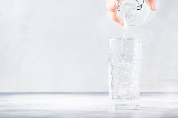 istock Clear water is poured from glass bottle into glass, gray background, selective focus 1156421556