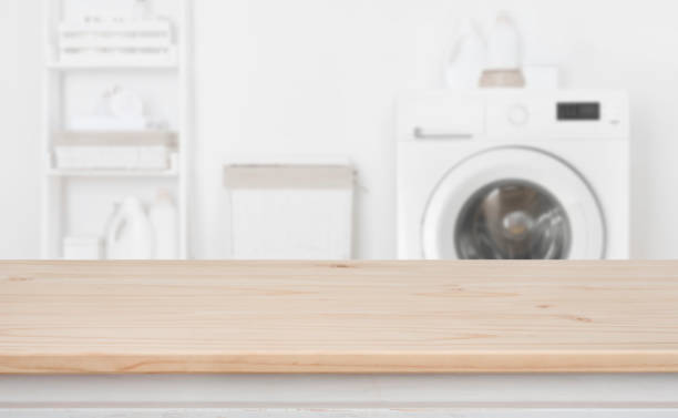 istock Wooden table in front of defocused washing machine and laundry 1156423228