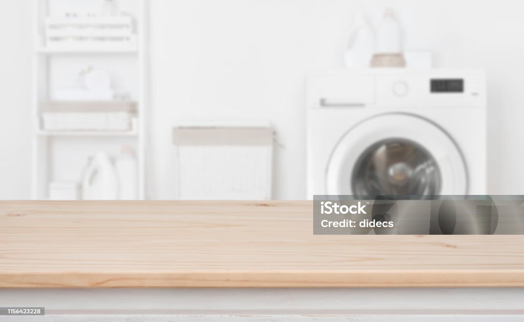 Wooden table in front of defocused washing machine and laundry Laundry Stock Photo