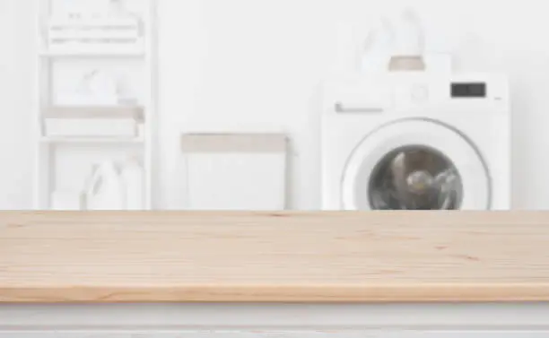 Photo of Wooden table in front of defocused washing machine and laundry