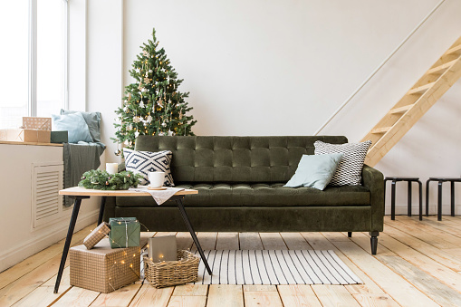Comfortable sofa standing in middle of stylish room beautifully decorated for Christmas celebration