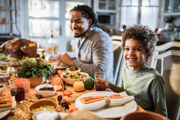 menino preto feliz que tem a refeição da acção de graças com seu pai na tabela de jantar. - dining table dinner thanksgiving table - fotografias e filmes do acervo