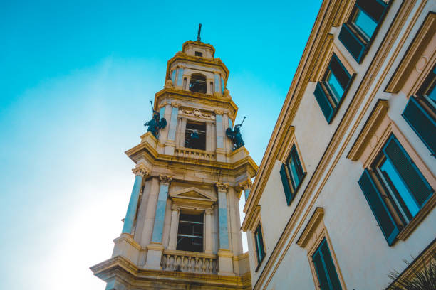 Church spire or bell tower with statues of angels blowing trumpets on the corners viewed from below against a blue evening sky