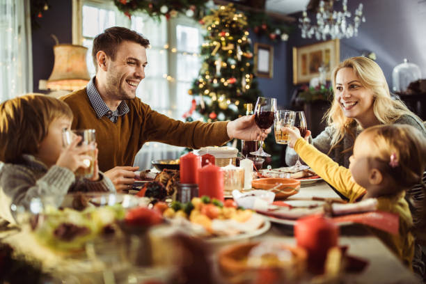 joven familia feliz brindando durante la cena de año nuevo en la mesa de comedor. - los niños y los padres brindis bebidas mientras almuerza fotografías e imágenes de stock