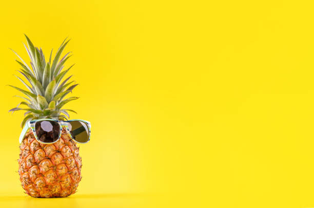 Creative pineapple looking up with sunglasses and shell isolated on yellow background, summer vacation beach idea design pattern, copy space close up