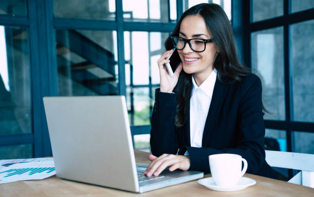 istock Charming happy business women dressed in full suit using smartphone and laptop while sitting in modern office 1156432206
