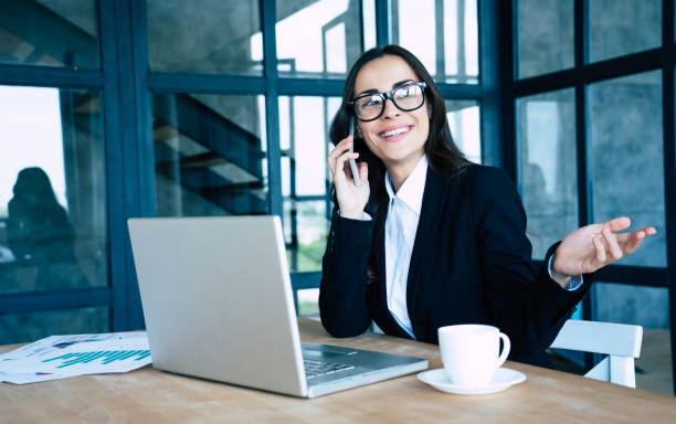 istock Charming happy business women dressed in full suit using smartphone and laptop while sitting in modern office 1156432244