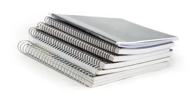 Stack of the different exercise books with wire spiral binding at selective focus on a white background
