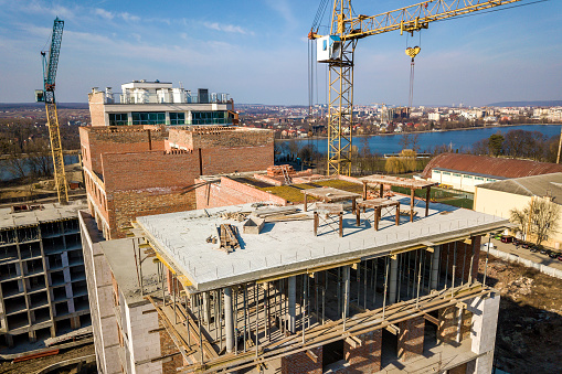 Apartment or office tall building under construction, top view. Brick walls, scaffolding and concrete support pillars. Tower crane on bright blue sky copy space background. Drone aerial photography.