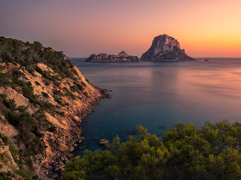 View of bucolic and beautiful landscape during the sunset, from the cliff, of the Cala D'hort natural park on the island of Ibiza, Spain. In the background the famous islets of Es Vedra, Es Vedranell and the calm and relaxing Mediterranean sea