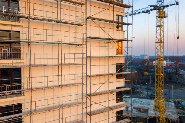 istock Apartment or office tall unfinished building under construction. Brick wall in scaffolding, shiny windows and tower crane on urban landscape and blue sky background. Drone aerial photography. 1156446434