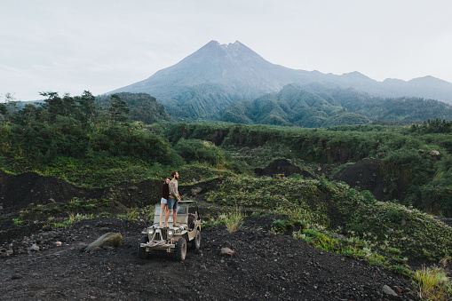 Scenic aerial view of couple on  old fashioned SUV on the background of Merapi volcano on Java, Indonesia