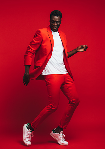 Full length od handsome young african man dancing on red background. Man in stylish red outfit showing some dance moves.