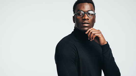 Handsome young african man in black polo t-shirt and eyeglasses looking away against gray background.