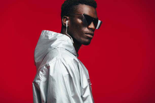Stylish young african male model Handsome young african man in silver hooded shirt, sunglasses and earphones. Funky young african american guy against red background. fashion model men male sunglasses stock pictures, royalty-free photos & images