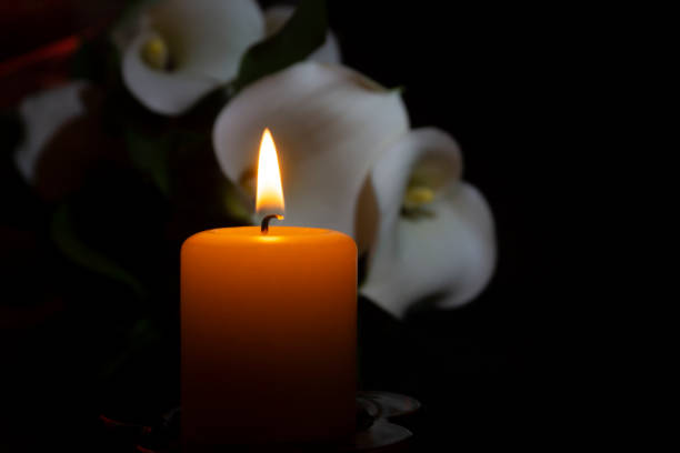 primo passo di fiamma arancione candela e fiori di giglio - necrologio immagine foto e immagini stock