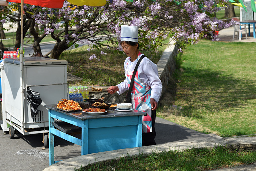 Pyongyang, North Korea - May 1, 2019: Female seller of roast meat shown in the Taesongsan Funfair. Is an amusement park located in Taesong-guyok