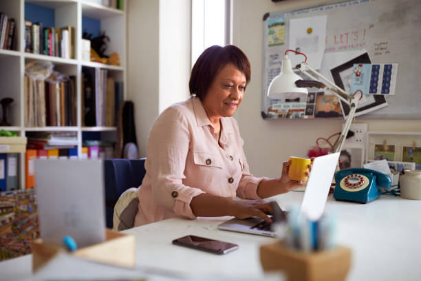 uśmiechnięta dojrzała kobieta z laptopem pracującym w domowym biurze - working at home mature adult small business laptop zdjęcia i obrazy z banku zdjęć