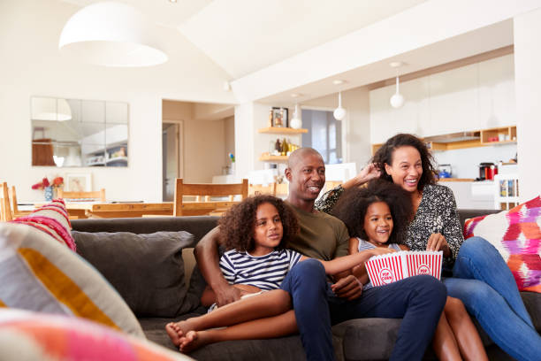 rodzina siedzi na kanapie w domu jedzenie popcorn i oglądanie filmu razem - movies at home zdjęcia i obrazy z banku zdjęć