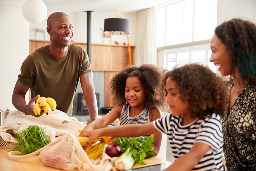 Family Returning Home From Shopping Trip Unpacking Plastic Free Grocery Bags