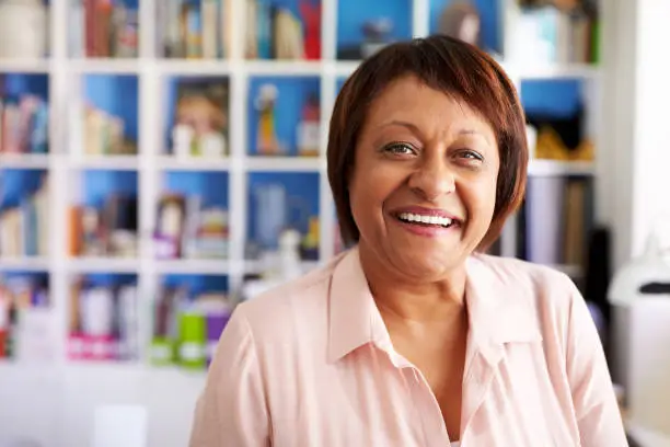 Portrait Of Smiling Mature Woman In Home Office By Bookcase