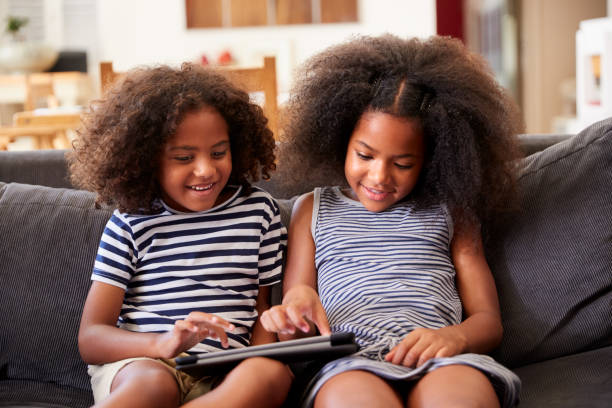 istock Brother And Sister Sitting On Sofa At Home Playing With Digital Tablet 1156462906