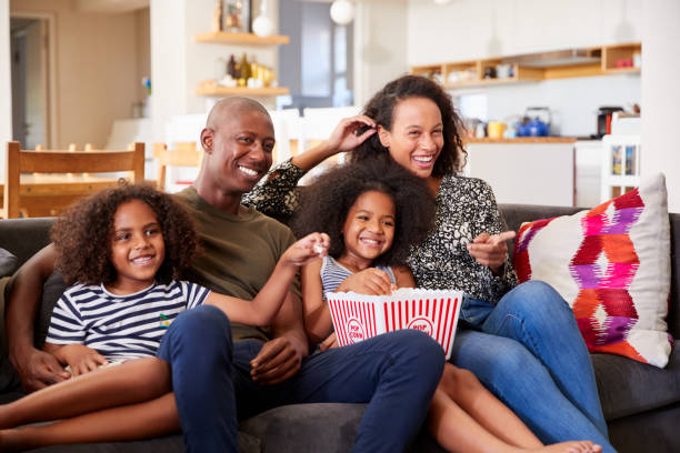 famiglia seduta sul divano a casa a mangiare popcorn e guardare film insieme - home movie foto e immagini stock